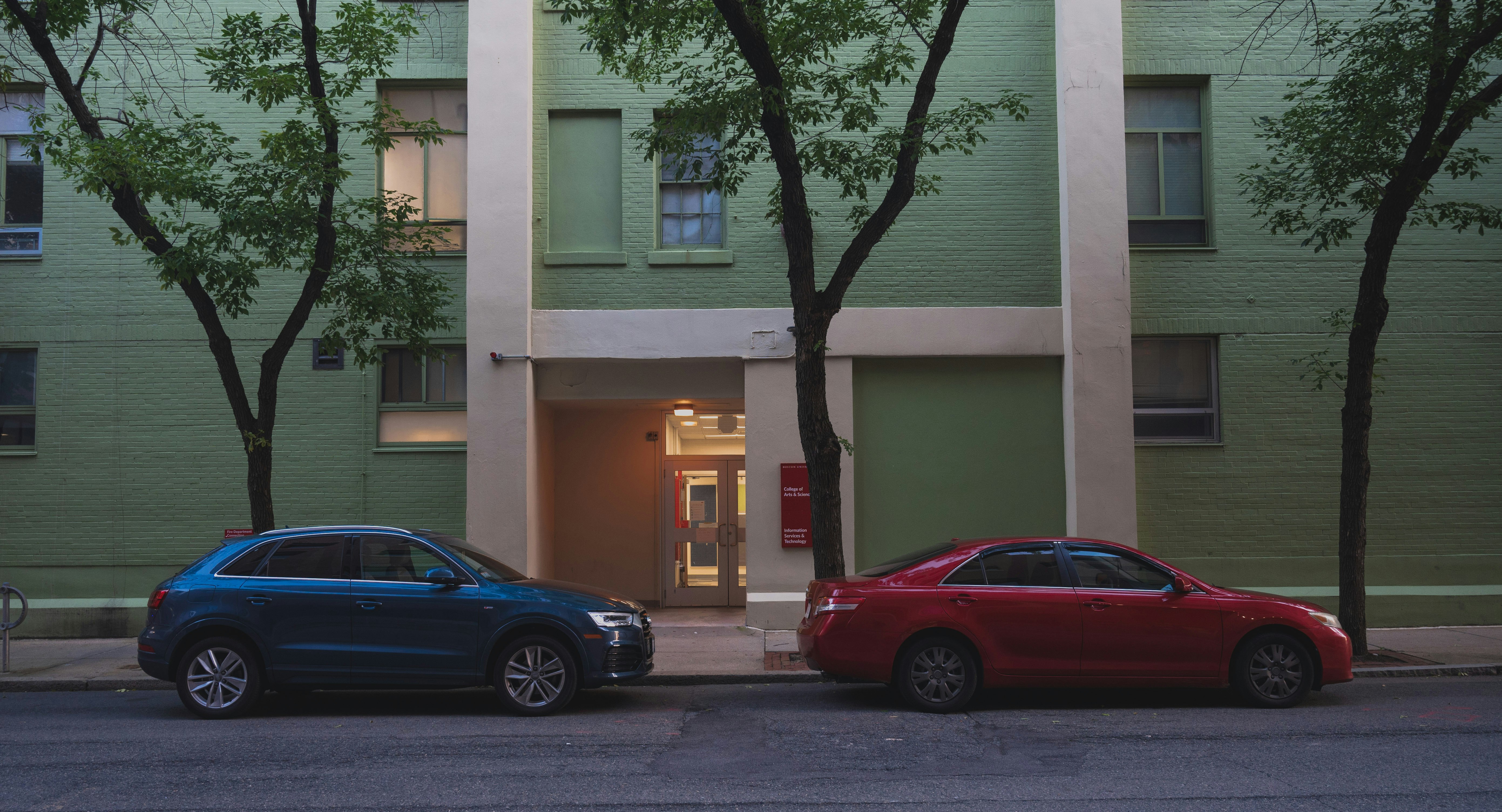 black sedan parked beside white concrete building during daytime